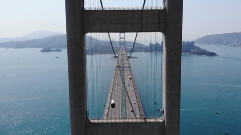 Aerial camera fly through open frame of two-legged pylon, impressive lengthwise perspective of large suspension bridge. Unusual view of Lantau Link towards Hong Kong International Airport