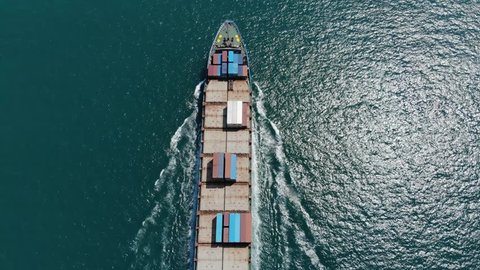 Easy loaded container ship during return trip, top-down aerial tracking shot. Cargo carrier move at sea channel with several containers on board, view of vessel fore and open deck from height