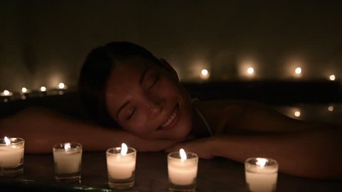 Beautiful woman relaxing in hot bath tub. Steam is coming out from water in Jacuzzi. Beauty spa is decorated with lit candles.