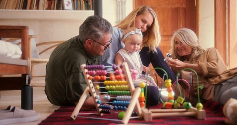 Grandparents, adult daughter and granddaughter sitting on living room floor and playing with toys