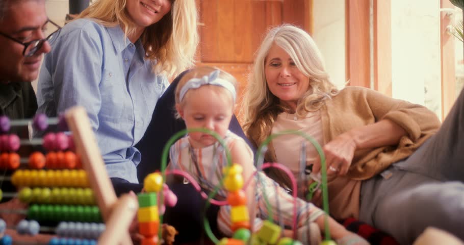 Happy grandparents sitting on floor and playing with little baby granddaughter at home
