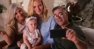 Three-generation family with grandparents, daughter and grandchild sitting on sofa and video calling at home