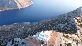 Aerial drone bird’s eye view video of iconic small chapel of Profitis Ilias built on a cliff overlooking picturesque port of Kamares, island of Sifnos, Cyclades, Greece