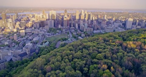 AERIAL: Flying over Mont Royal looking out to Montreal city skyline at sunset, Canada.