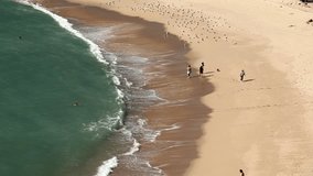 Moving video of a beach with people walking along the coast and swimming in the sea.