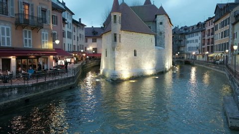 Annecy, France - April 13, 2018: Camera tilt up from old town canal water to reveal Palais De L'isle prison lighted at night