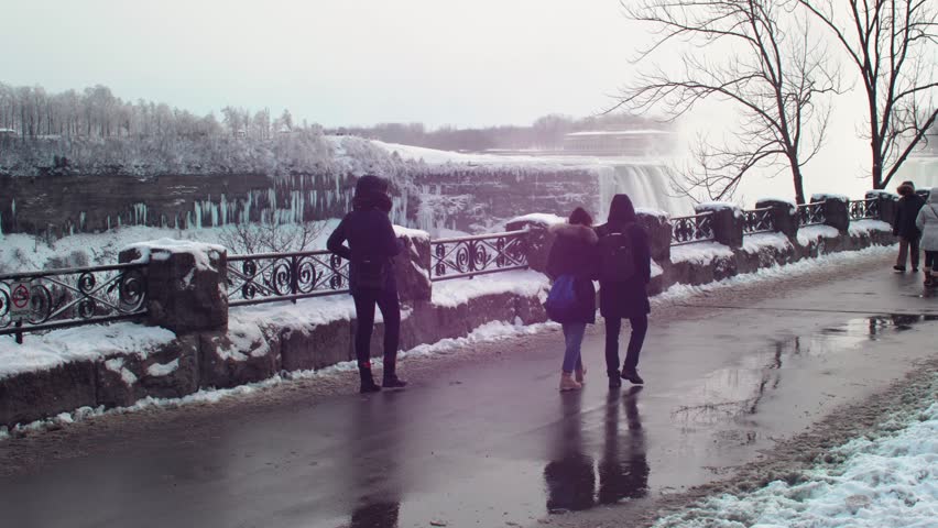 Slow motion panning right shot of People walking the niagara parkway on a really cold day with Niagara falls in the background.