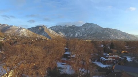Slow drone shot nearly missing the tree opening up to a community lying just beneath a beautiful backdrop of mountains and snow.