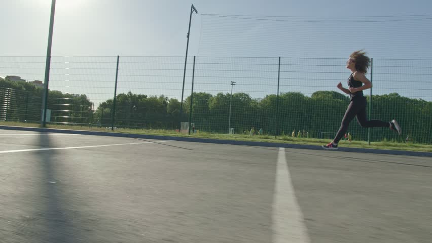 Woman girl running at a stadium, summer sunny day.