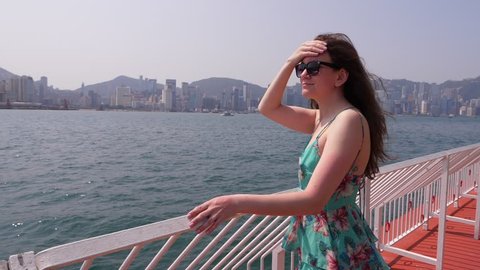 Young woman feel hot and burn from sunlight ultraviolet radiation, cover forehead by hand. Bright sun light at city embankment, lady look to waterfront panorama