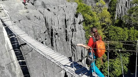 Tsingy de Bemaraha, MADAGASCAR - MAY 18, 2018: Hiker tourist walks over suspended rope bridge over gorge in national park