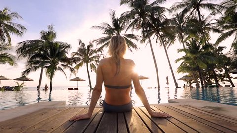 Woman relaxing by the pool in a luxurious beachfront hotel resort spa at sunset enjoying perfect beach holiday vacation, traveling footage