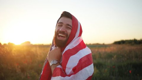 Funny man holding the flag of America in the field look at camera smile talk happy attractive beautiful design man nature american athlete traveller friends body male model slow motion sunset
