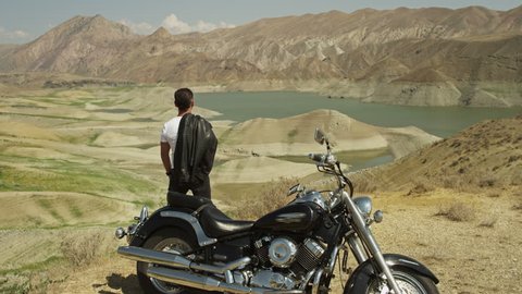 Biker standing near motorcycle on mountain  and looking, watching or enjoying beautiful view of nature. Shot on RED EPIC Digital Cinema Camera.