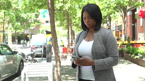 African American woman reacts to a message on her phone and is visibly upset. 