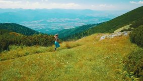 Running woman on the top of mountain. Runner is jogging in summer sunny day around trees and mountains background under sun light with blue sky, Drone 4K Video