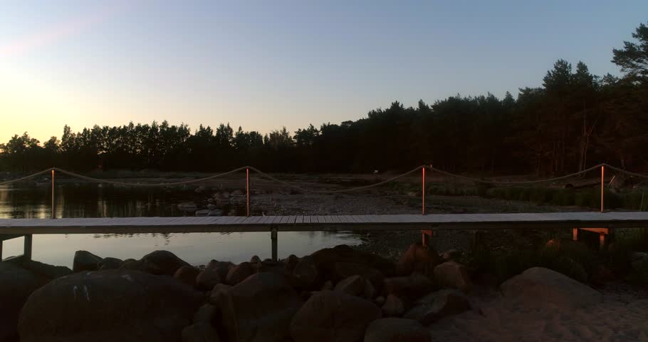 Woman standing on wharf, C4K aerial view around a girl on a harbor, at a beach at the baltic sea, on a sunny summer evening dusk, Hanko, Uusimaa, Finland