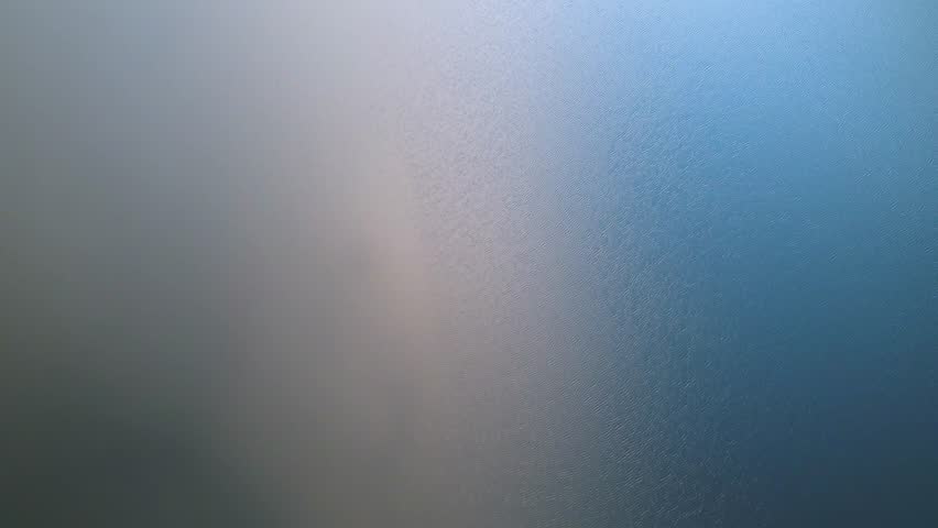 4K Teal and orange water reflections from an overhead flyover on silky smooth lake.