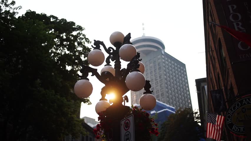 In Gastown, Vancouver, the setting sun shines behind a street light with the Harbour Centre in the background