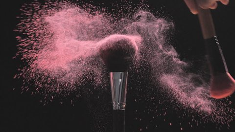 Make-up brushes with pink powder on a black background in slow motion