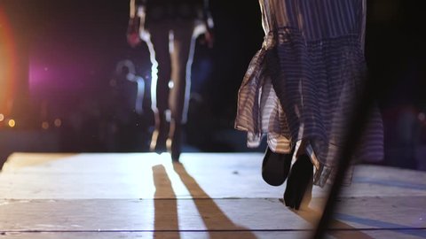 fashion week, Catwalk models in elegant long dresses on high heels walk along podium in bright searchlight lighting