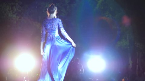 defile professional model in luxurious evening dress on catwalk in lighting spotlights on fashion show