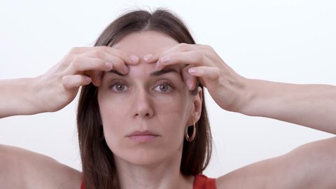 Close up of brunette woman doing horizontal movement of fingers over the eyebrows to reduce wrinkles between the eyebrows. Isolated on the white background.