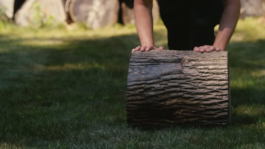 A man rolls a thick log towards the camera