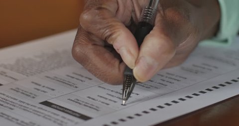 African American woman's hand filling in a voter ballot for a general election and voting