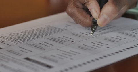 Senior black hand voting on a voter paper ballot in an election