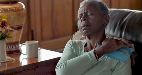 Elderly senior black woman in her 50s or 60s in pain puts an ice pack on her shoulder to relieve the tension and discomfort