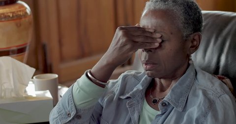 Elderly senior black woman rubbing her forehead to relieve headache pain from a sinus cold, allergies, or flu symptoms