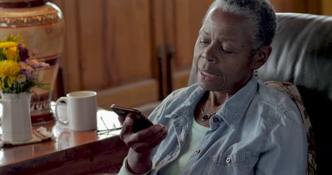 Annoyed senior black woman in her 50s or 60s answering her mobile phone and being bothered by the caller