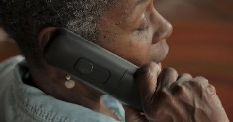Older black woman in her 50s or 60s with short black and gray hair talking on a cordless landline phone - OTS