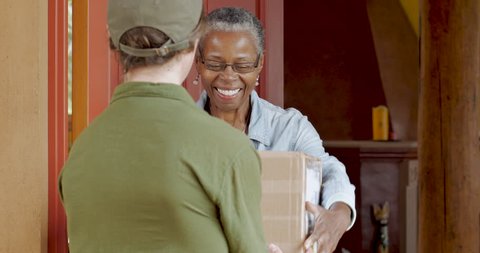 African American elderly woman receiving a home deliver package and digitally signing it's proof of delivery from a postal courier man in a uniform