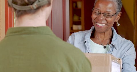 Happy smiling attractive elderly senior black woman receiving a home delivery package delivery box and signing electronic delivery device app from courier