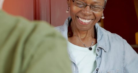 Happy smiling senior black woman home owner receiving a delivery package from a postal courier and signing a digital proof of delivery signature