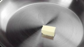 Butter is melting in a hot metal frying pan.