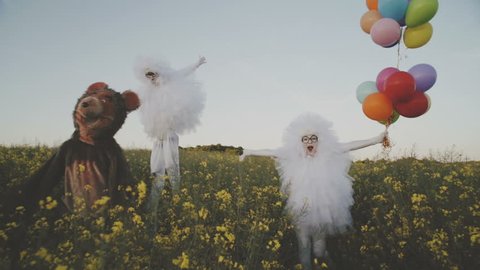 Two funny clowns mime in white air suits and with colored balloons walk around the field and have fun with a cheerful bear. HD