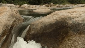 High definition panning action rugged mountain river waterfalls panoramic scene, with rushing white water cascading around large pebbles, boulders. Stock footage HD video clip.