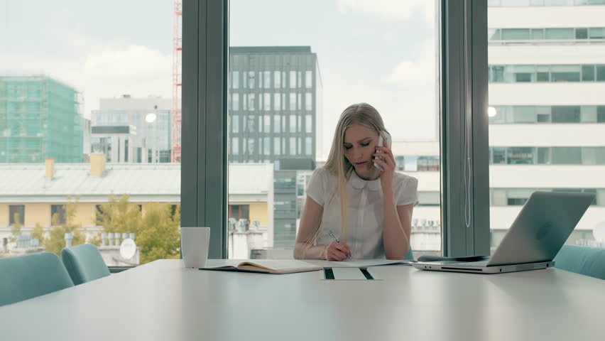 Serious woman working in light office room. Elegant modern businesswoman with laptop and papers at long table in conference light room having phone call. Royalty-Free Stock Footage #1013575751