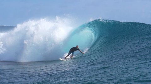 SLOW MOTION, CLOSE UP: Experienced male surfer gets almost swept by a big crystal clear barrel wave curling over his head while surfing in beautiful French Polynesia. Rider catches an awesome wave.