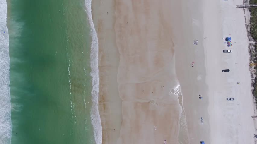 This is a top down shot of Daytona Beach with its beautiful emerald waters, and people playing on its shoreline.