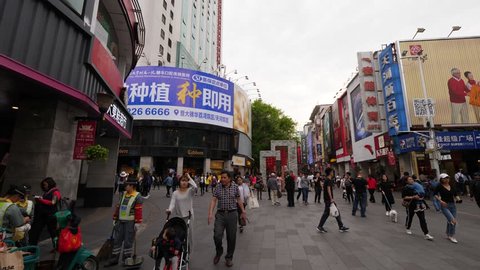 GUANGZHOU, CHINA - MARCH 14, 2018: Buildings covered with advertising banners and sign boards at shopping street, unidentified people stroll along Beijing Lu pedestrian road at Guangzhou, slow motion