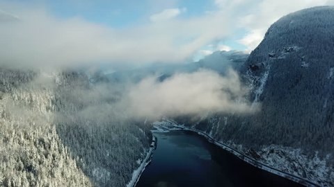 Aerial footage of flying through a cloud in the mountains over a lake during the winter while it was snowing lightly