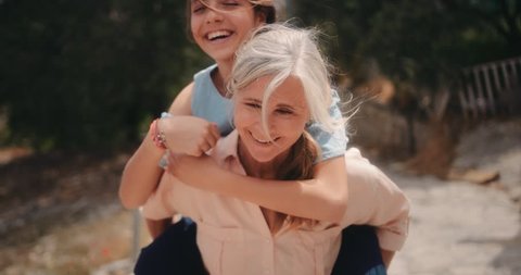 Grandmother and teenage granddaughter having fun with piggyback ride on summer holidays in Mediterranean village