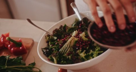 Close-up of woman adding fresh pomegranate to gourmet Mediterranean salad while preparing healthy lunch Stock Video