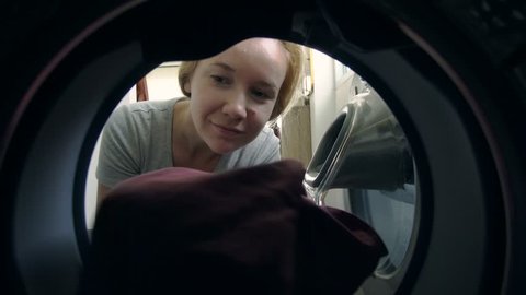 Young Caucasian Woman Loading Dirty Clothes into Washing Machine. Household Chores and Duties Concept.View from Inside