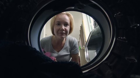Young Caucasian Woman Loading Dirty Clothes into Washing Machine. Household Chores and Duties Concept. View from Inside