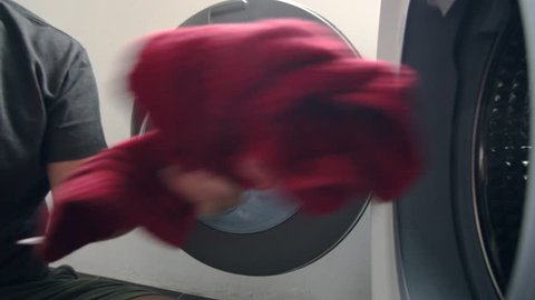 Young Caucasian Man Loading Dirty Clothes into Washing Machine. Household Chores and Duties Concept